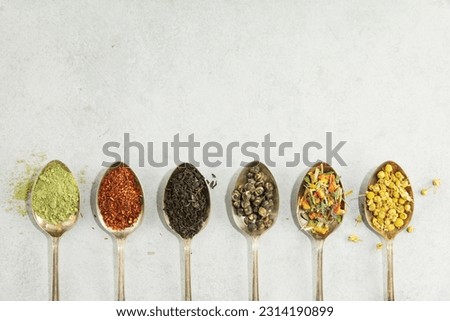 Different types of tea in vintage spoons. Flat lay, top view on concrete background. Matcha, rooibos, black, green, herbal mix and camomile tea. Copy space