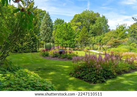 The different types of trees and shrubs form a nice backdrop to this lawn with a large vase surrounded by Astilbe in an arboretum in Rotterdam, the Netherlands