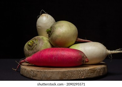 Different varieties of radish on a black background. Long red radish next to white radish. Delicious and healthy vegetables. Vegetarian food.