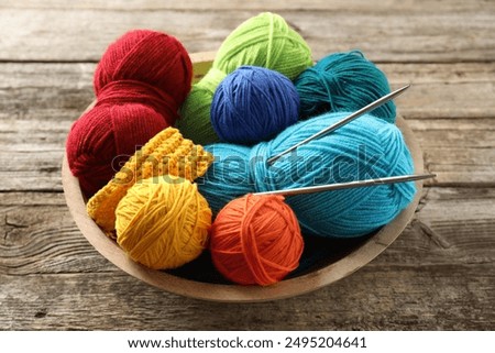 Different yarns, knitting needles and pattern sample in bowl on wooden table, closeup