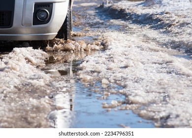 Difficult driving conditions on roads in the village. Melting dirty snow with water, car on the background, slowly moving - Shutterstock ID 2234796351
