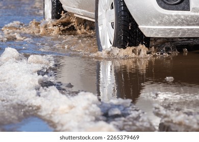 Difficult driving conditions on roads in Spring. Car moving on road with melting snow through puddles - Shutterstock ID 2265379469