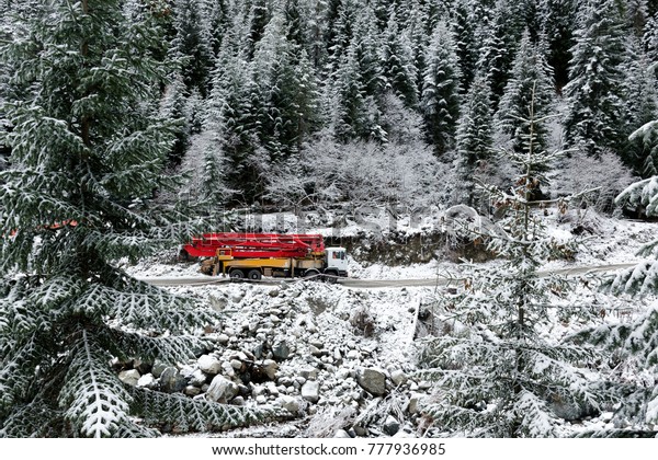 Difficult working\
conditions - a truck with a crane rides a mountain road, among\
snow-covered high spruce\
trees.