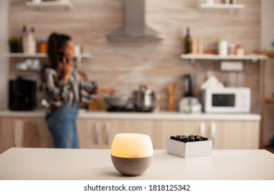 Diffuser spreading essential oils in kitchen and woman relaxing. Aroma health essence, welness aromatherapy home spa fragrance tranquil theraphy, therapeutic steam, mental health treatment