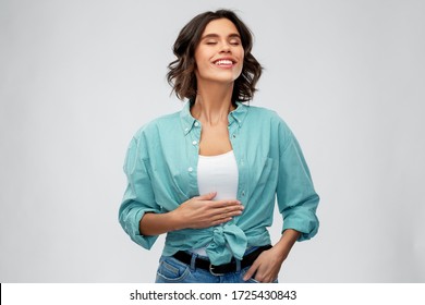 digestion, eating people concept - happy smiling full young woman in turquoise shirt touching her tummy over grey background