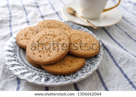 Digestive cookies biscuit on white vintage plate ceramic modern cup of tea in background on white tea towel. Selective focus food styling 