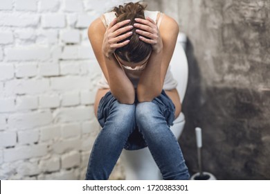Digestive Disorder. Woman Suffering From Constipation Sitting On Toilet In Restroom Indoors. Defecation Problem And Hemorrhoids Concept.