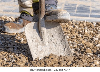 Digging gravel with a wide shovel on a construction site,The worker rests his foot on the shovel to push it into the gravel and scoop the material onto it.