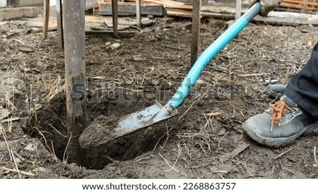 digging an old metal post out of rocky ground with a blue-handled shovel, digging an earthen hole to pull a post out of the soil, or to set up a post in a garden or yard