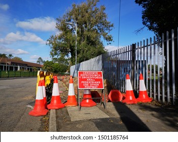 Digging the pavement up in a residential district to repair or replace water pipes with safety fencing, traffic cones and a welsh language bilingual warning sign.
