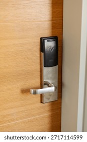 A digital access control system is installed on a wooden door. The device features a card reader and a handle. It is part of a secure entryway in an office building.