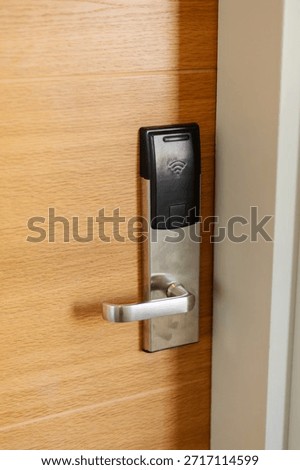 A digital access control system is installed on a wooden door. The device features a card reader and a handle. It is part of a secure entryway in an office building.
