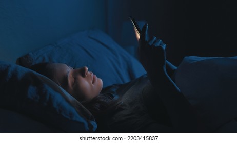 Digital Addiction. Tired Woman. Online Life. Sleepless Lady Laying Bed Scrolling Smartphone In Light Shadow Room Interior.