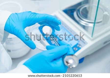 Digital analytical balance for accurate weighing of samples. Close up scientist hands in rubber gloves use metal spatula for weighing white powder of the substance.