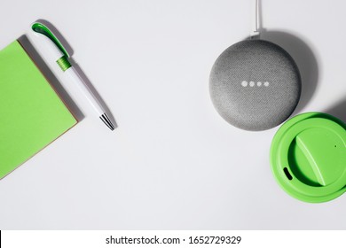 Digital Assistant concept. Flat lay of smart speaker with LED lights activated with cropped green notepad, pen and reusable coffee cup.