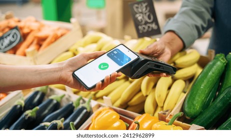 Digital Banking Concept: Shopper Using Cellphone with Contactless Payment Technology to Pay for Natural Goods at a Farmers Market. Street Vendor Holding an Electronic Payment and a Card Reader Device - Powered by Shutterstock