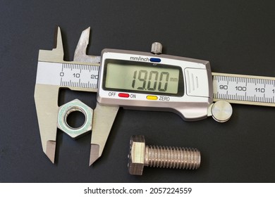 Digital caliper, or Vernier gauge, measuring a nut, on black background