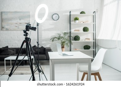 Digital Camera On Tripod Near Ring Lamp And Table With Laptop