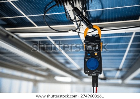 A digital clamp meter measures electrical current from photovoltaic panel wiring. The testing process helps technicians monitor solar energy system performance.