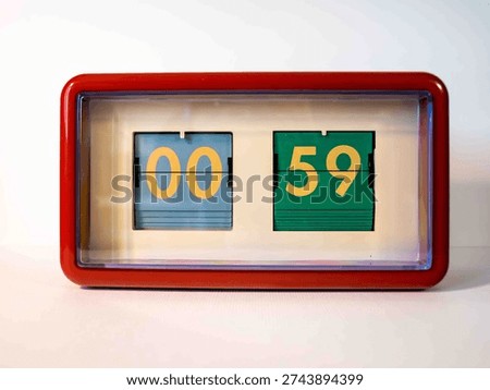 A digital clock shows the time as zero hours and fifty-nine minutes. The display features two sections in blue and green with clear numbers. The clock stands still, capturing a moment.