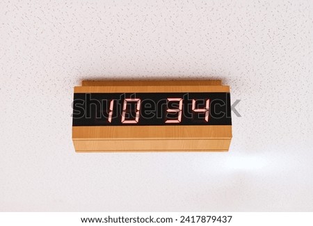 Digital clock time LED red number on black digital electric Brown wooden border stuck on white concrete wall. time symbol concept for celebrating the New Year. At Time 10.34 AM.
