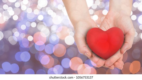 Digital composite of Close-up of female's hands holding heart shape over glowing bokeh