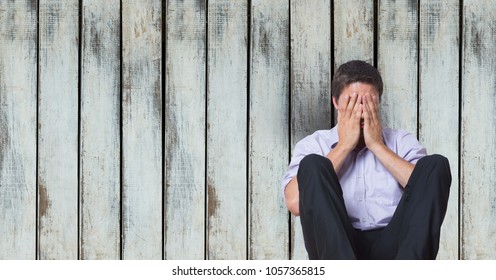 Digital composite of Depressed businessman covering face while sitting against wooden wall