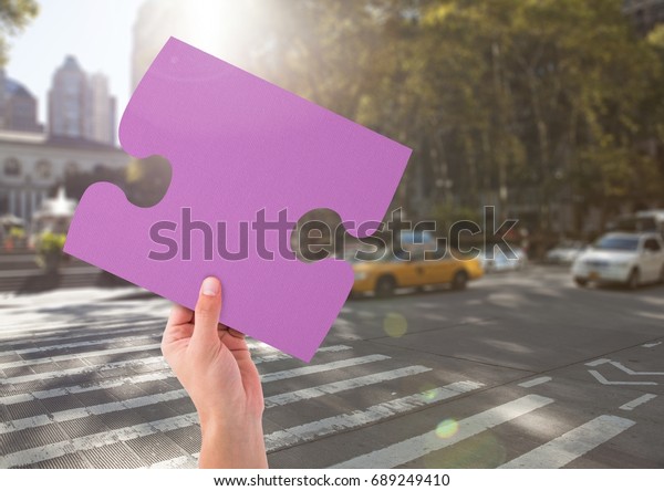 Digital composite of Hand holding jigsaw puzzle\
piece in city