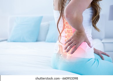 Digital composite of highlighted spine of woman with back pain at home - Shutterstock ID 660953398