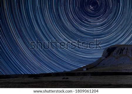 Digital composite image of star trails around Polaris with landscape of Norber Ridge and stone barn in Yorkshire Dales National Park