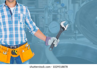 Digital composite of Midsection of worker holding wrench while standing against in factory