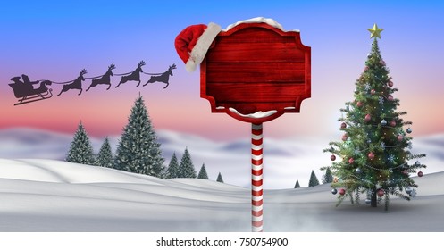 Digital composite of Wooden signpost in Christmas Winter landscape with Christmas tree and Santa's sleigh and reindeer's - Powered by Shutterstock