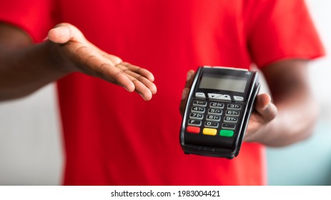 Digital Contactless Transaction. Cropped Closeup View Of African American Man In Red T-shirt Uniform Holding And Showing POS Machine, Selective Focus On Payment Dataphone Terminal, Blurred Background