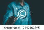 Digital copyright or patent concept. Author rights and patented intellectual property. Businessman holding a magnifying glass focuses on a copyright symbol surrounded by legal icons. trademark license