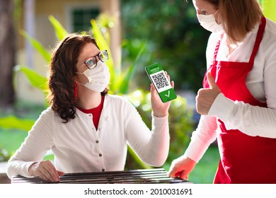 Digital covid-19 vaccination certificate on mobile phone. Coronavirus vaccinated people scan QR code on restaurant entrance. Negative test, completed vaccine and immunity proof for safe travel.
