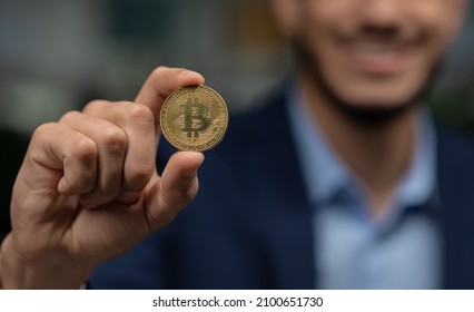 Digital cryptocurrency, trading on stocks and markets concept. Unrecognizable middle eastern businessman holding golden bitcoin and smiling, closeup of hand with coin. Panorama, selective focus - Powered by Shutterstock