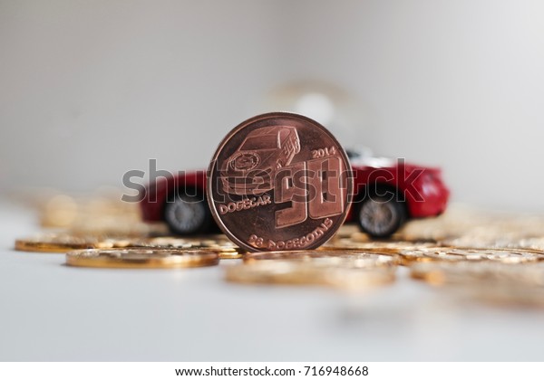 Digital currency physical metal brass dogecoin coin\
near red cabriolet car.