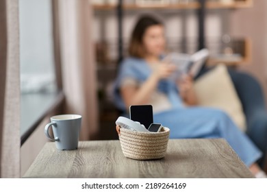 digital detox and leisure concept - close up of gadgets in basket on table and woman reading book at home - Shutterstock ID 2189264169