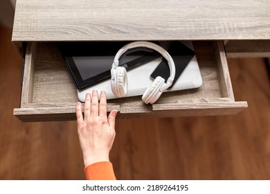 Digital Detox And Technology Concept - Close Up Of Hand And Different Gadgets In Desk Drawer At Home