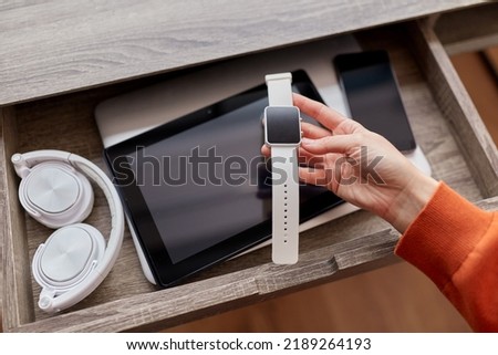 digital detox and technology concept - close up of hand holding smart watch and different gadgets in desk drawer at home