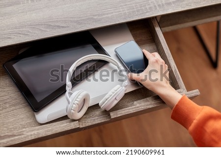 digital detox and technology concept - close up of hand with smartphone and different gadgets in desk drawer at home