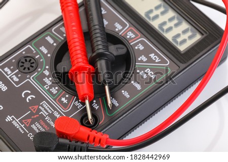 Digital electrical tester multimeter in black case isolated on white background. Digital multimeters have a numeric display, can measure voltage, current and resistance. Close up.