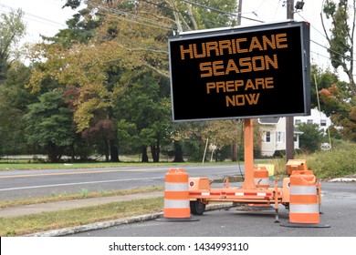 Digital electronic mobile road sign that says Hurricane Season prepare now, on the side of a tree lined neighborhood road