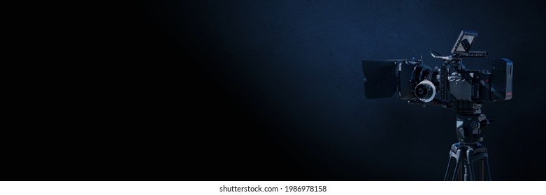 Digital film camera in the dark on blue concrete wall background. Video camera with copy space for film production, tv or broadcast media banner.