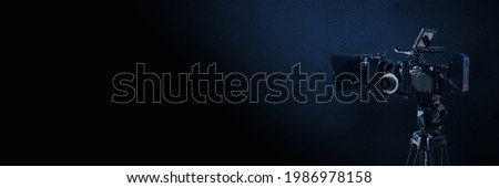 Digital film camera in the dark on blue concrete wall background. Video camera with copy space for film production, tv or broadcast media banner.