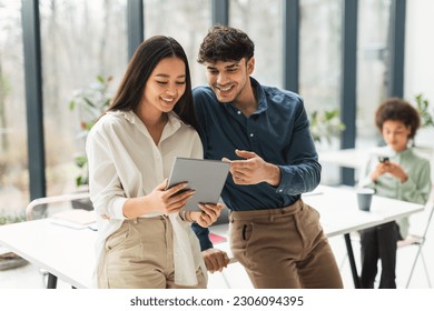 Digital Fun At Workplace. Cheerful Mixed Business Coworkers Couple Using Tablet Computer Together Surfing Internet And Discussing Corporate News In Modern Office. Teamwork And Interaction - Powered by Shutterstock