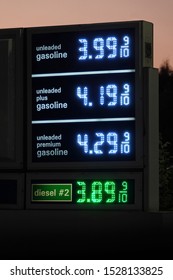 A Digital Gas Station Sign Displays Current Fuel Prices Next To A Road In The United States During The Evening.