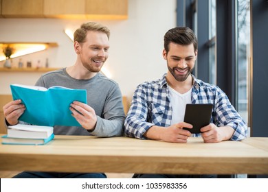 Digital generation. Joyful positive nice man sitting together and smiling while reading books