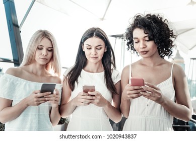 Digital Generation. Nice Attractive Young Women Standing Together And Using Their Smartphones While Not Paying Attention To Each Other