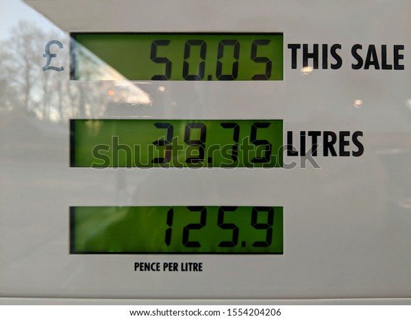 Digital, green and black, liquid crystal display (LCD)\
of a shiny white enamel petrol pump with a reflection of trees and\
early morning sun and the price, number of litres & pence per\
litre displayed 